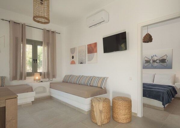 A modern bedroom with a bed, a sofa, a TV, and artwork on the wall. - Voulisma Hills (Agios Nikolaos)