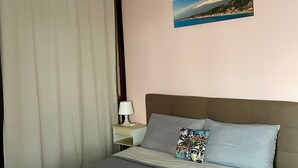 A neatly made bed with grey linens and two rolled towels, a bedside lamp, and a painting of a coastal landscape on the wall. - Apartment with terrace Etna and sea view near central station (Catania)