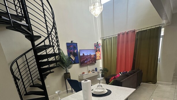 A modern kitchen with a central island, a black spiral staircase, and a flat-screen TV mounted on the wall. - Rainbow Retreat near the heart of kingston (Kingston)