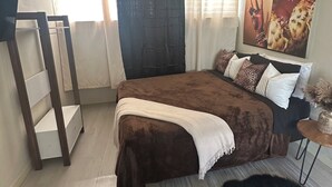 A bedroom with a bed, a ceiling fan, a window with curtains, a wall-mounted picture, and a small table with a vase. - Rainbow Retreat near the heart of kingston (Kingston)