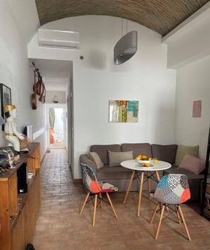 A modern living room with a sofa, two chairs, a small table with fruit, and a TV on a wooden cabinet.