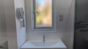 A bathroom with a white sink, a mirror, and a window with frosted glass. - Quiet self contained apartment with free parking, close to Hospital (Torquay)