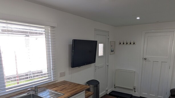 A kitchen with a wooden countertop, stainless steel sink, and a dishwasher. There is a television mounted on the wall, a white door, and a window with blinds. - Quiet self contained apartment with free parking, close to Hospital (Torquay)