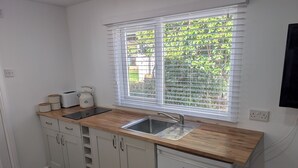 A kitchen with a double sink, wooden countertop, white cabinets, and a window with blinds. - Quiet self contained apartment with free parking, close to Hospital (Torquay)