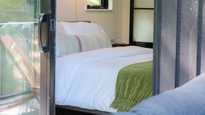 A bedroom with a bed, a nightstand, a lamp, and a window. - Modern Cabin | Hot Tub + Forest Views | 2 BR 2 BA (Logan)
