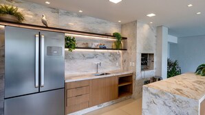 Eine moderne Küche mit Edelstahl-Kühlschrank, Holzschränken, Marmorarbeitsplatten und Beleuchtung unter den Schränken.
