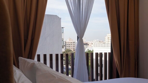 Ein Hotelzimmer mit Bett, Vorhängen und Blick auf Gebäude durch ein Fenster.
