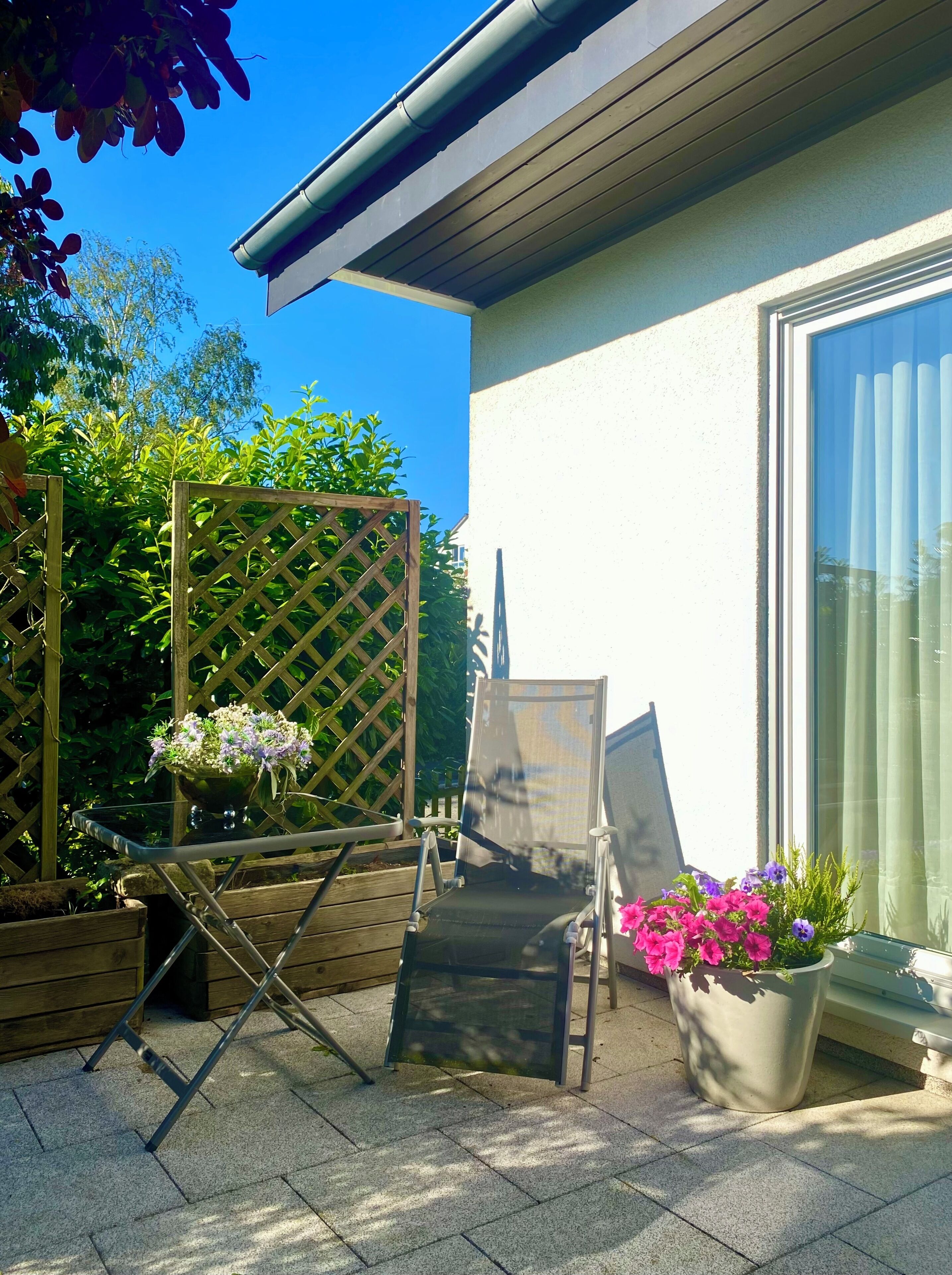 Eine Terrasse mit Klappstuhl, einem kleinen Tisch und Topfpflanzen.