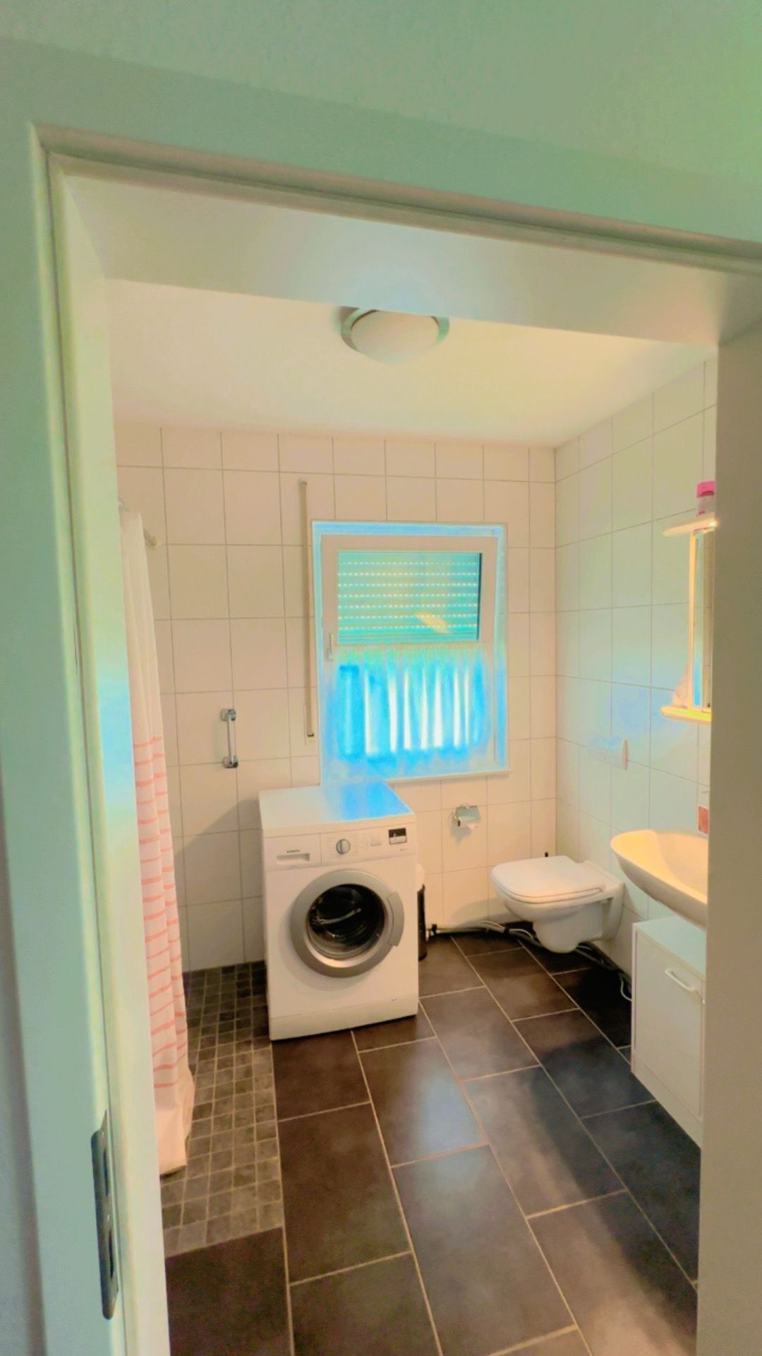 Un baño pequeño con lavadora, inodoro y ventana con persianas.