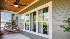 A covered porch with a ceiling fan, a swing seat, and large windows. - Stylish 4BR near Avondale Restaurants | Sleeps 10 (Birmingham)