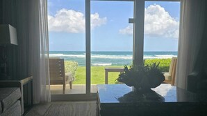 A room with a view of the ocean, a sofa, a table with a plant, and a chair. - Luxury Beachfront 3-Bedroom Condo | Ocean View (sint maarten)