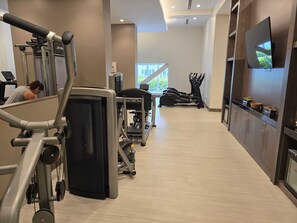 Ein modernes Fitnessstudio mit Cardiogeräten, Gewichten und einem Fernseher an der Wand.