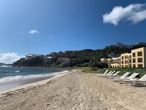 Une plage avec des chaises longues blanches et un bâtiment doté de nombreux balcons.