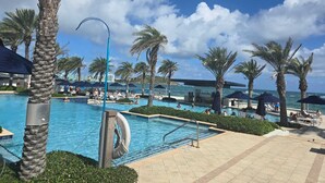 A resort pool area with palm trees, lounge chairs, and a clear view of the ocean. - Luxury Beachfront 3-Bedroom Condo | Ocean View (sint maarten)