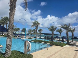 Ein Poolbereich einer Ferienanlage mit Palmen, Liegestühlen und Blick auf den Ozean.
