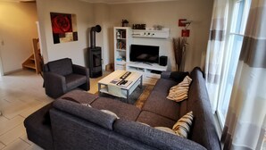Un salon comprenant un canapé, un fauteuil, une télévision, une bibliothèque et une cheminée.