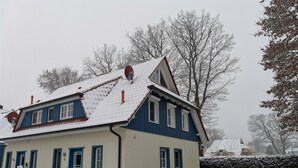 Une maison à deux étages, à la façade bleue et blanche, avec un toit enneigé et une boîte aux lettres bien visible.