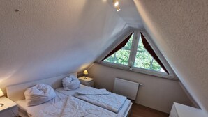 Une chambre à coucher avec un lit, une table de chevet, une lampe, une fenêtre avec des rideaux et un radiateur.