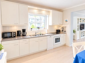A modern kitchen with white cabinetry, a built-in oven, a microwave, and a coffee maker. - MeerZeit - cozy vacation apartment in Zingst - only 200 meters to the beach (Zingst)