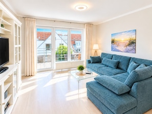 A modern living room with a sofa, a television, and a glass coffee table. - MeerZeit - cozy vacation apartment in Zingst - only 200 meters to the beach (Zingst)