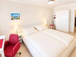 A hotel room with a large bed, a desk with a chair, a wardrobe, and a picture on the wall. - MeerZeit - cozy vacation apartment in Zingst - only 200 meters to the beach (Zingst)
