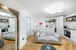 A compact living space with a sofa, a dining table, a kitchen area, and a large mirror. - Crown Street Suite 1 - Grampian Lettings (Aberdeen)