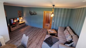 Un salon doté d’un plancher en bois, d’un canapé gris, d’un meuble TV en bois et d’un luminaire fixé au mur.