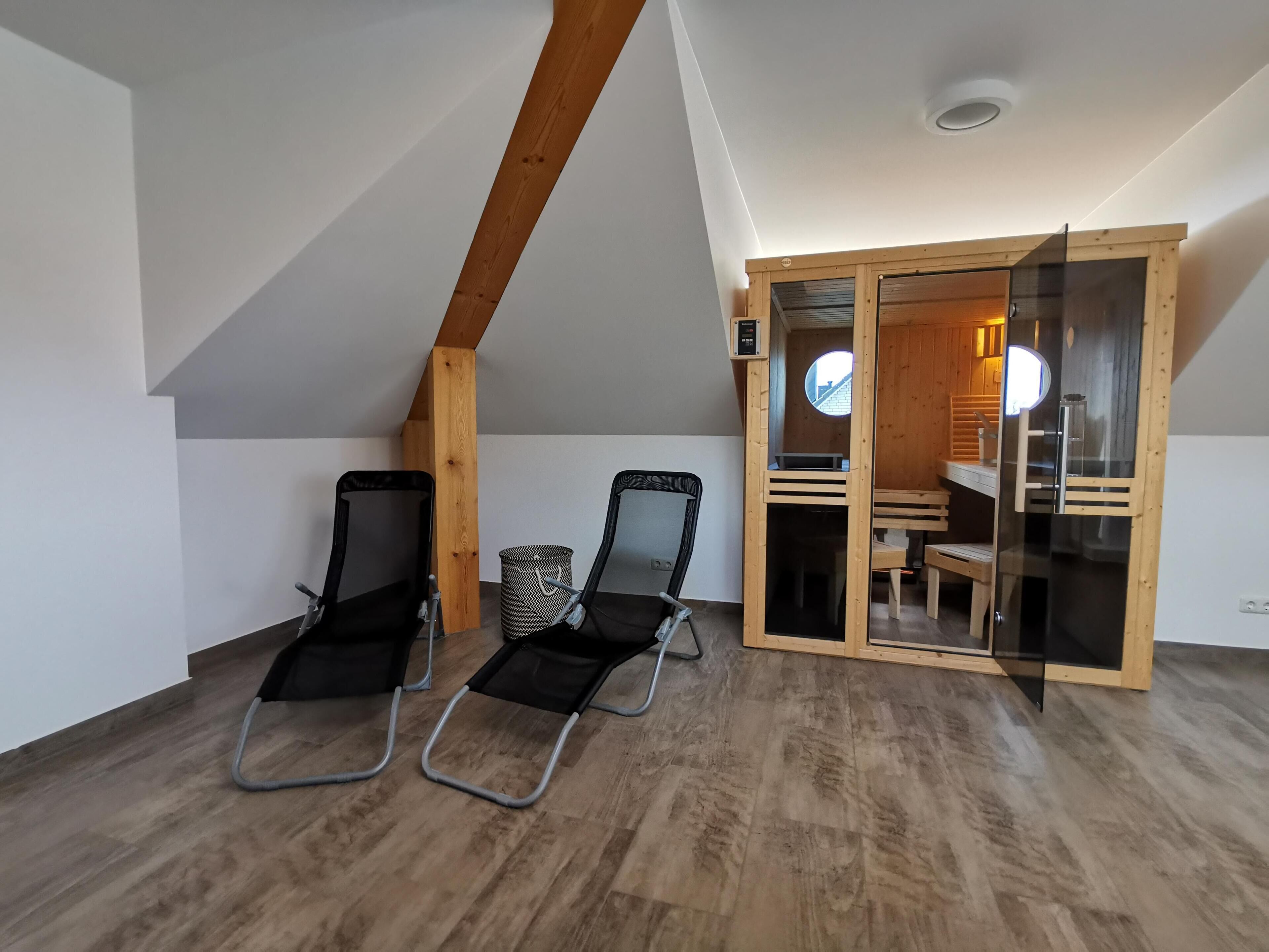 A room with a sloped ceiling, two reclining chairs, a small trash bin, and a wooden-framed sliding door leading to a dining area.
