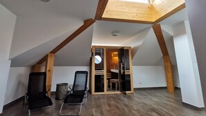 Ett rymligt sovrum på entresolplan med ett takfönster, synliga träbjälkar, en inbyggd garderob och en sittgrupp med stolar.