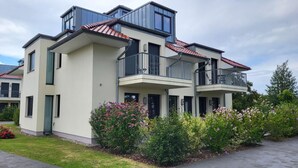 Un moderno edificio residencial de varios pisos con balcones, techo plano y un jardín cuidado.
