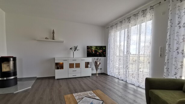 Una sala moderna con una mesa de centro de madera, un sofá verde, un mueble blanco para entretenimiento y un televisor montado en la pared.
