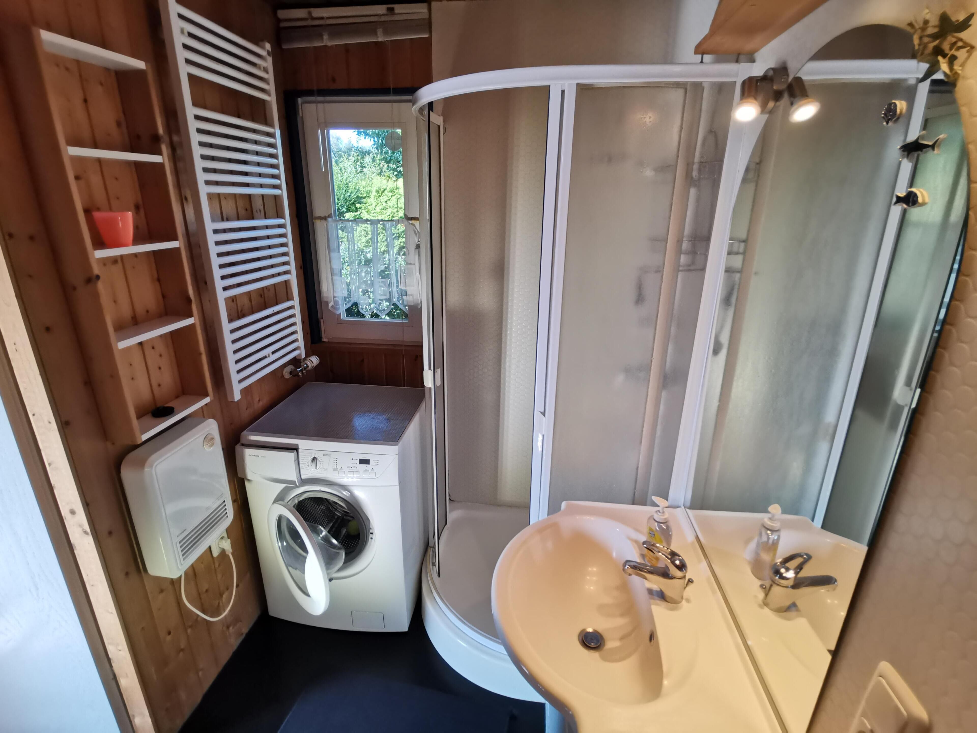 Une petite salle de bain équipée d’un lave-linge, d’un lavabo avec miroir et d’une cabine de douche.