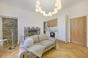 A modern living room with a sofa, a glass table, a stone wall, a fireplace, and a kitchen area with cabinets and a wooden door. - Crown Street Suite 2 - Grampian Lettings (Aberdeen)