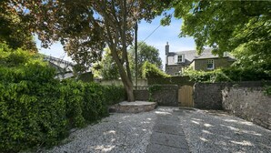 Un camí de grava que condueix a una porta de fusta, envoltat per una paret de pedra i vegetació abundant.