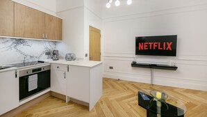 Una cuina moderna amb forn integrat, cafetera i torradora. Un televisor de pantalla plana muntat a la pared mostra el logotip de Netflix.