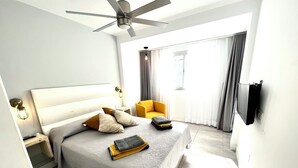 Ett modernt hotellrum med en stor säng, en takfläkt, en tv som är monterad på väggen och ett fönster med gardiner.