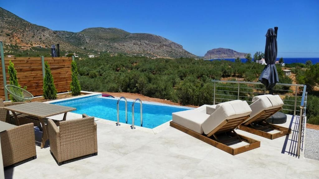 A pool area with lounge chairs and a table, surrounded by greenery and mountains in the background.