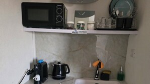 A compact kitchen with a microwave, coffee maker, kettle, and a small refrigerator.