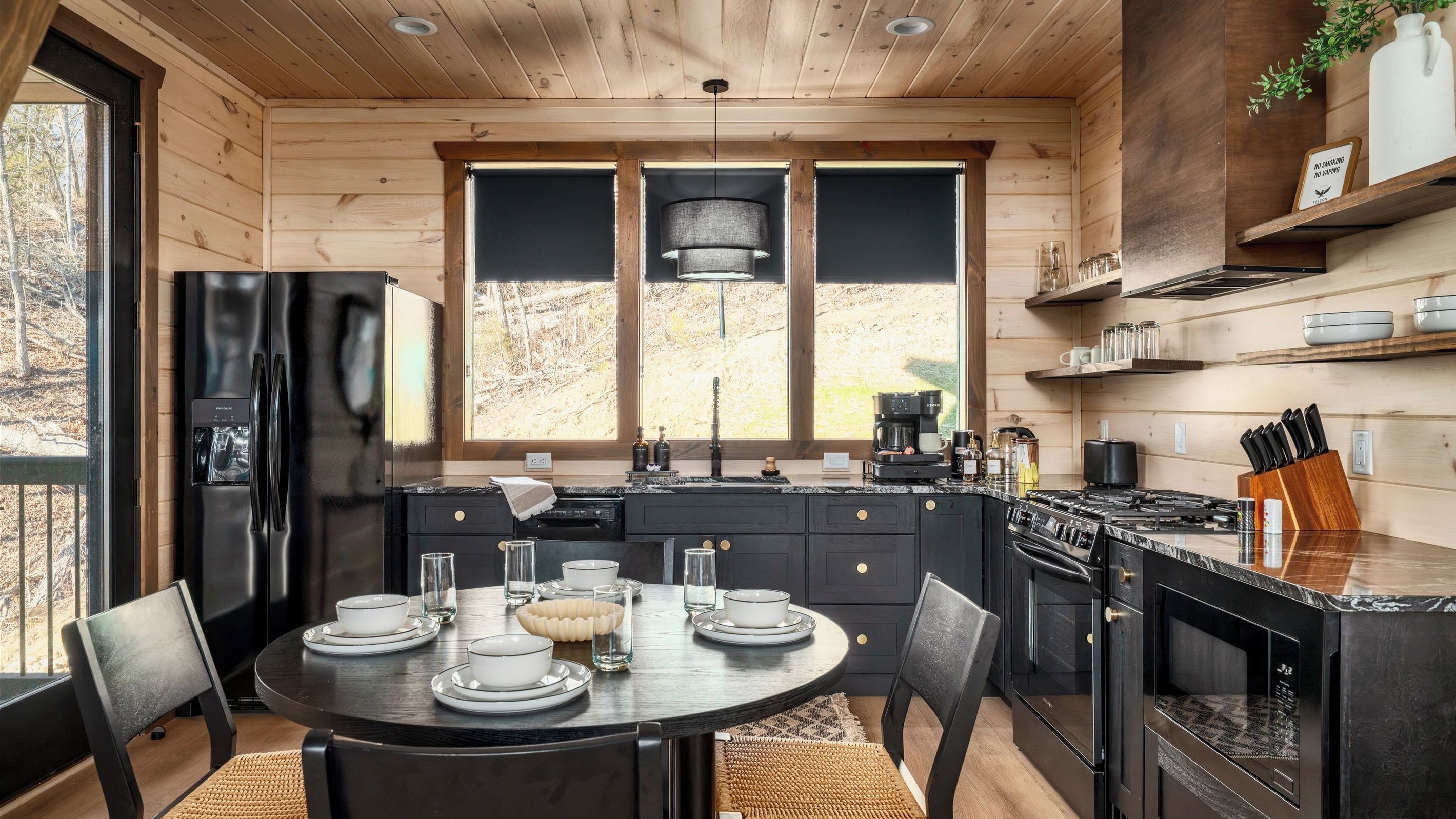 Une cuisine moderne dotée d’un îlot central, d’appareils électroménagers noirs et offrant une vue sur l’extérieur.