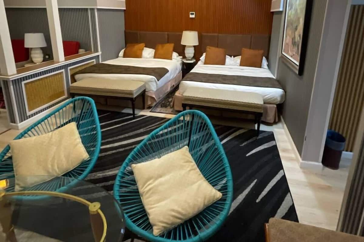 Quarto de hotel com duas camas, um ventilador de teto, aparelho de ar condicionado e uma janela grande.