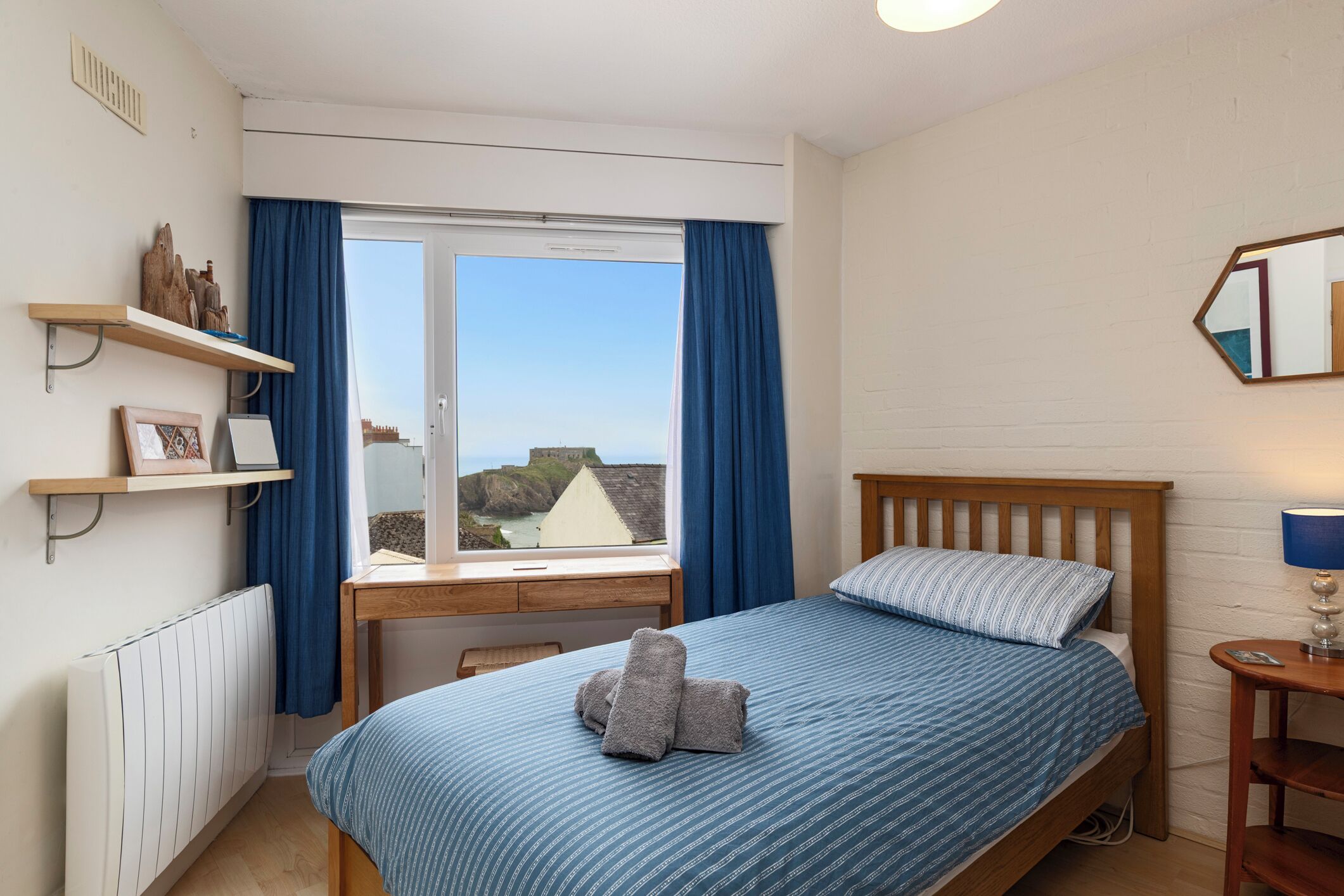 Une chambre à coucher avec un lit, une fenêtre avec des rideaux, une table de chevet, une lampe et une vue sur l’extérieur.