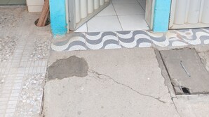 En dörröppning med ett metallgaller, ett klinkergolv med en dekorativ kant och ett betongunderlag med ett avlopp.