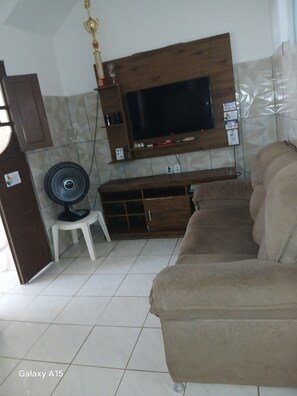 A living room with a sofa, a TV mounted on the wall, a fan, and a cabinet. - Cozy house in the center of Maragogi, pets allowed. (Maragogi)