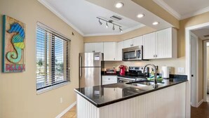 A modern kitchen with white cabinets, a stainless steel refrigerator, a microwave, and a red coffee maker. - Casa Bella A in Fort Myers Beach (Fort Myers Beach)
