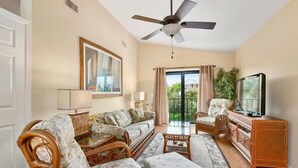 A spacious living room with a ceiling fan, a sofa set, a television, and a balcony with a view. - Casa Bella A in Fort Myers Beach (Fort Myers Beach)
