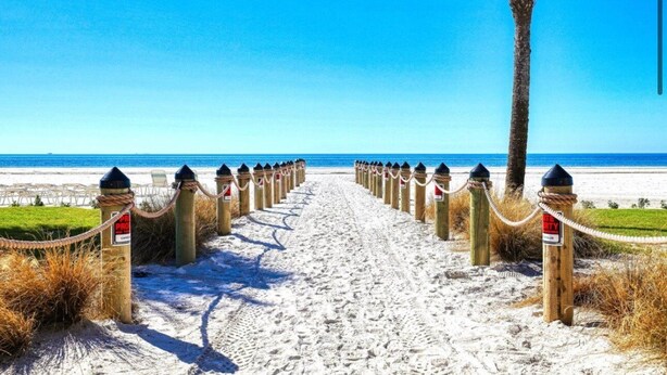 Ein Weg durch das Sand am Strand, gesäumt von Holzbalken und Seilen, der zum Meer führt.