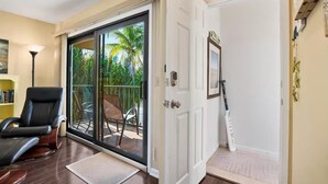 Una habitació amb una porta corredissa de vidre que dona a un balcó amb mobiliari exterior i palmeres.