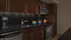 A modern kitchen with dark wooden cabinets, a stainless steel range hood, a built-in microwave, and a coffee maker. - Resort with 2 bedrooms and AC in lovely Marco Island (Marco Island)