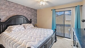 Een slaapkamer met een bed, een plafondventilator, een raam met gordijnen en uitzicht op buiten.
