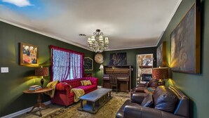 Een woonkamer met een rode bank, een piano, een kroonluchter en een groot schilderij aan de muur.